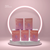 Five boxed A’Lei Beauty Chameleon makeup sponges stacked on a round pedestal against a pink background